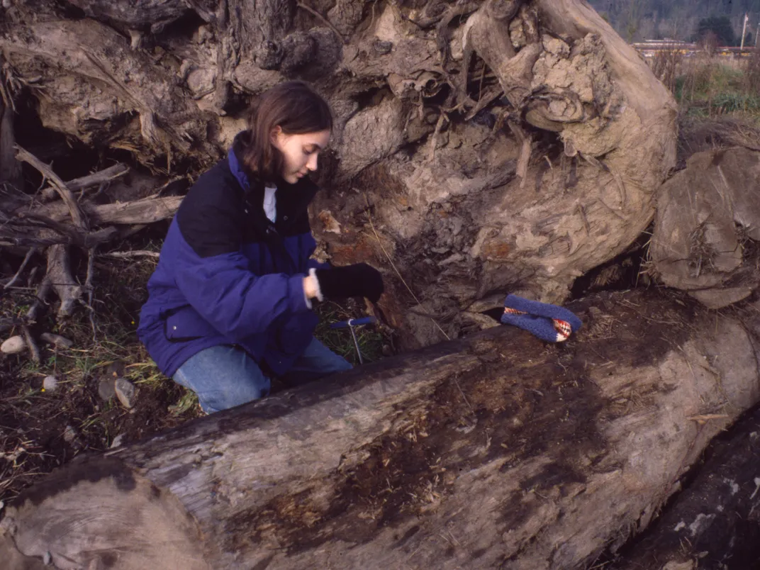 a woman in a blue jacket and jeans kneels in front of a subfossil tree