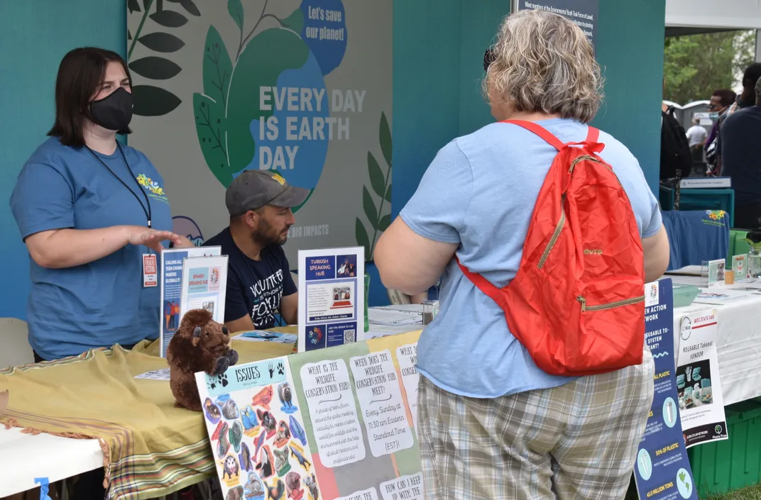 A teen speaks to a visitor at a table covered in information about the Global Co Lab Wildlife Hub's activities.