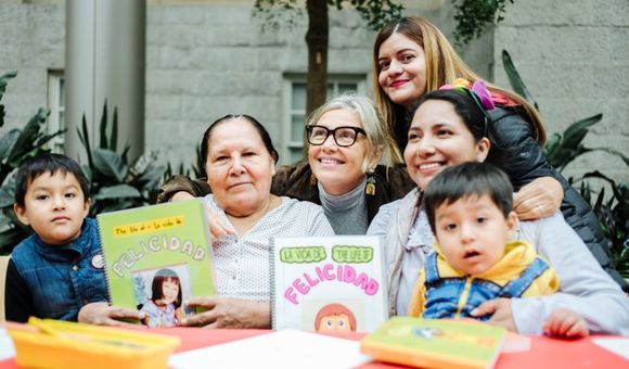 Woman smiles at the center of a group with young children and their mothers showcasing books they created