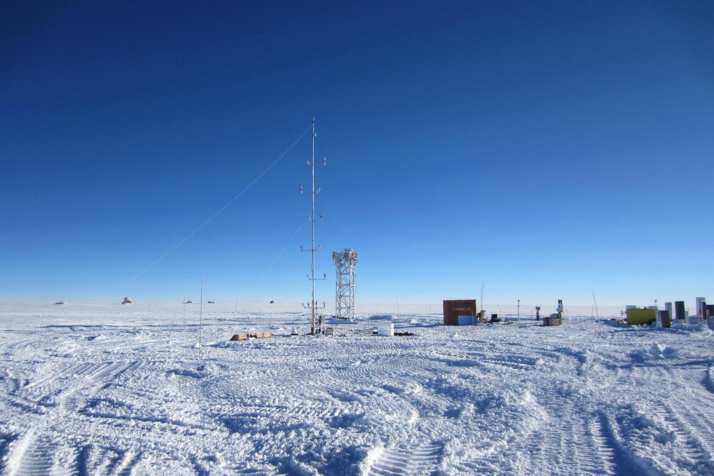 A view of Dome A site during daytime: a large expanse of snow, blue sky, and two metal structures rise out of the ground