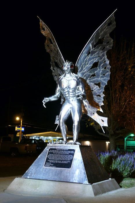The same Mothman statue at night, gleaming under a spotlight.