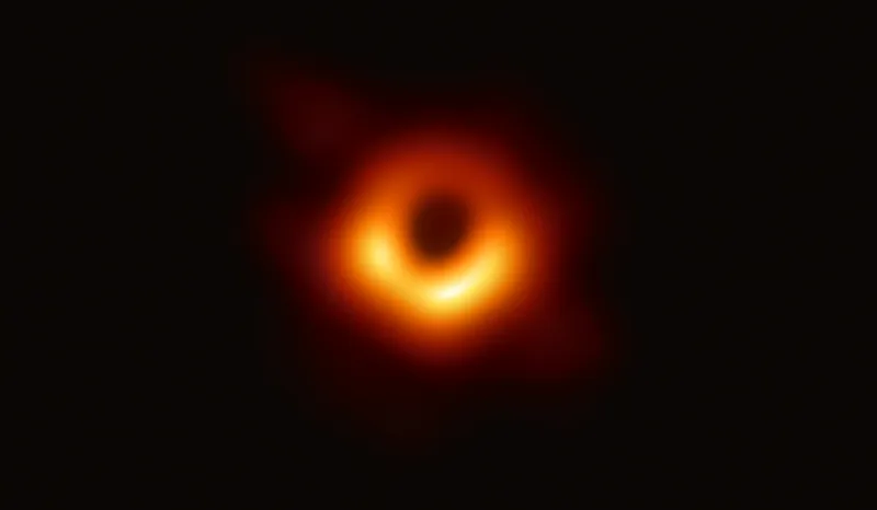 There is a black spot in the middle of the photo. It is surrounded by a bright orange ring that is brightest in the bottom half of the circle. The rest of the photo is an all black background.