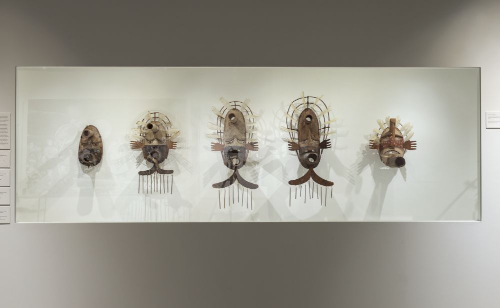 Five masks hanging side-by-side on a white wall. 