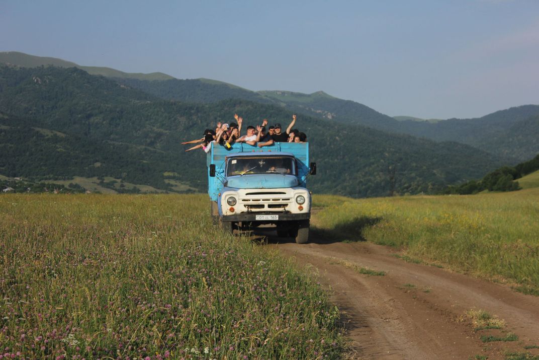A blue truck filled with people drives through a green field.