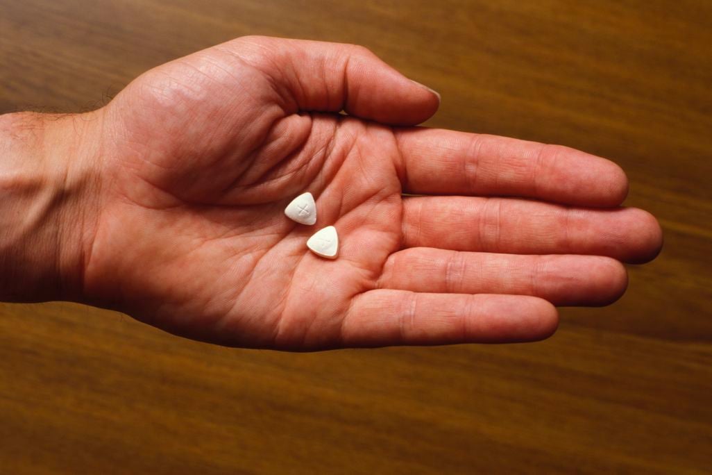 A person's open hand holding two triangle-shaped pills