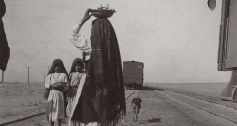 An Isleta woman and her children sell goods alongside a train track, circa late 1880s to early 1900s