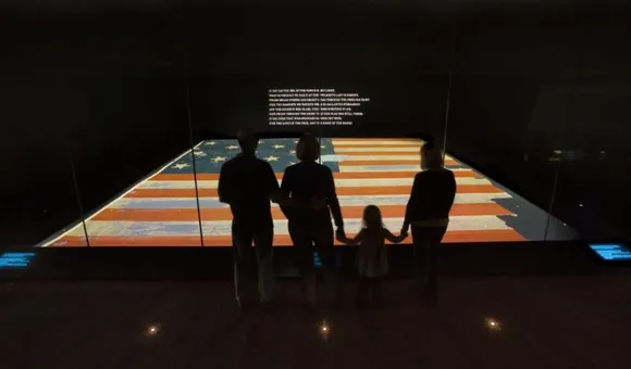 Visitors look at the Star Spangled Banner. It is dimly lit in its gallery at the museum.
