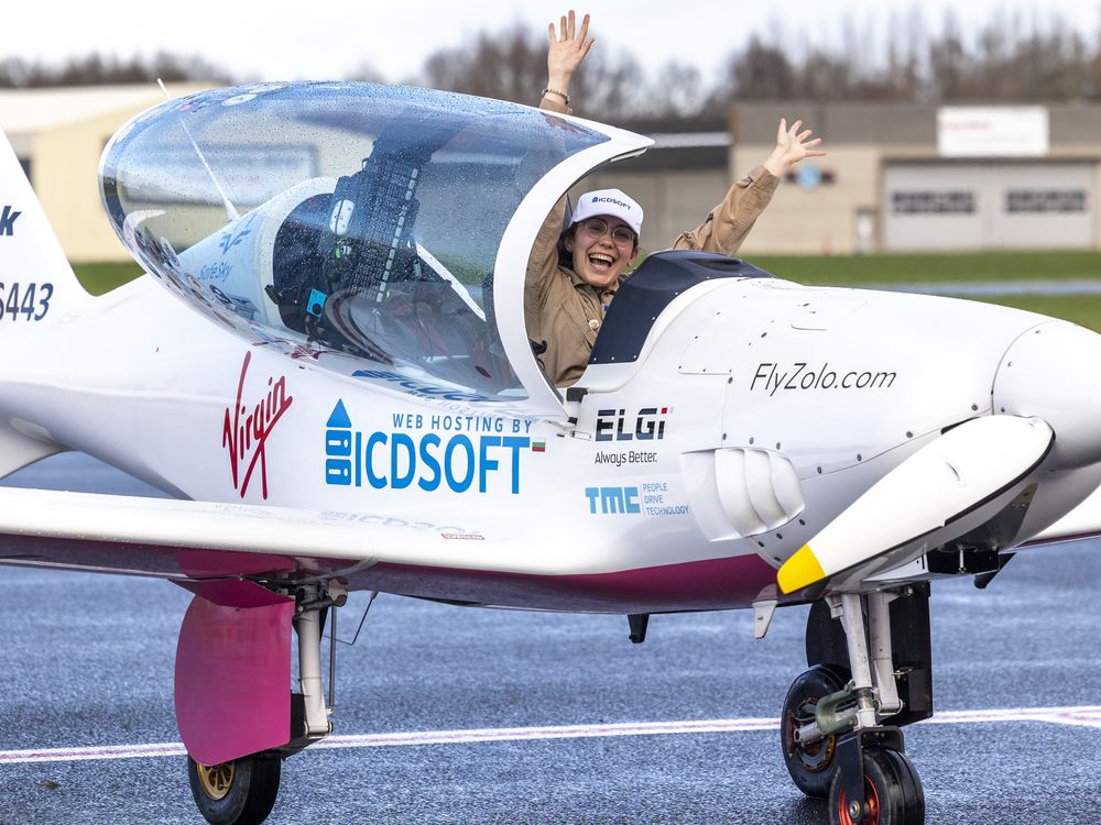 Young teenage girl with glasses and baseball cap extends her hands in excitement inside cockpit of landed plane