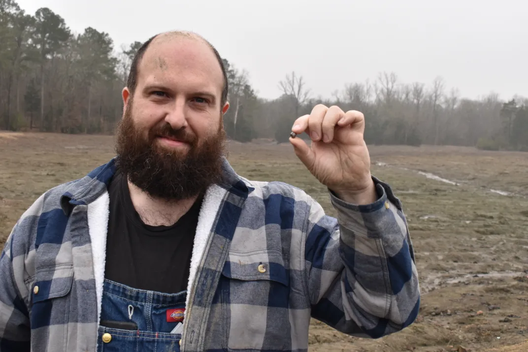 Balding man with dark beard holding up his hands to show off small rock