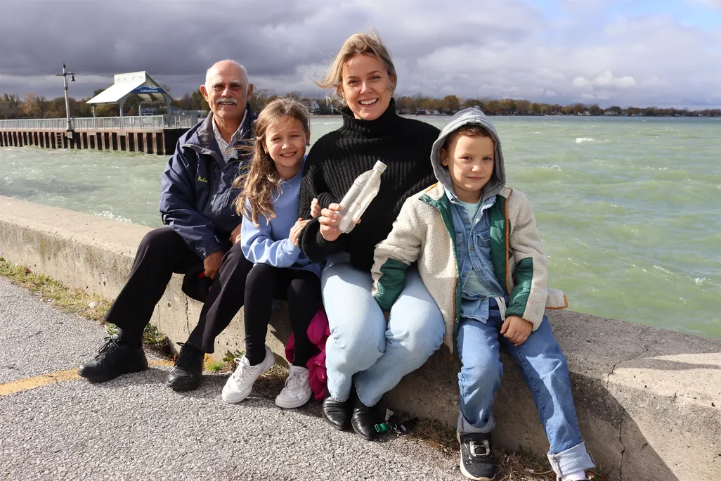 A man, two children and a woman sitting next to a body of water