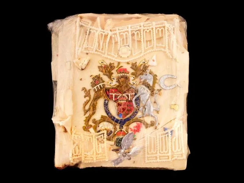 A closeup view of the cake slice, which is a square piece, yellowish, with cracked but intricate icing on top and a knight, gold leaf, and a laced icing border