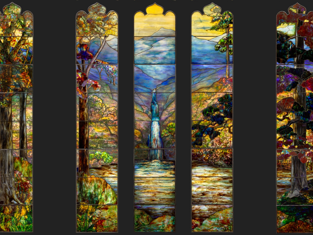 Five thin panels of stained glass, two on either side and three grouped closely together, depict a colorful landscape with blue mountain in the background and a waterfall flowing into a yellow green pond