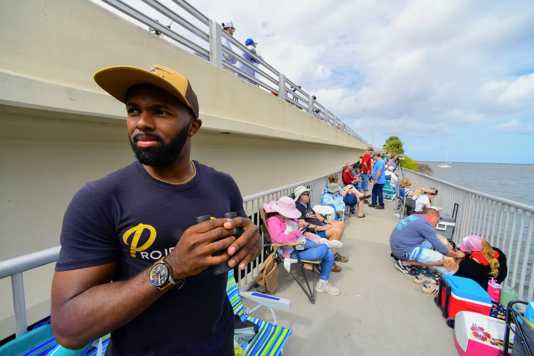 a man stands on a bridge in front of several people in folding chairs