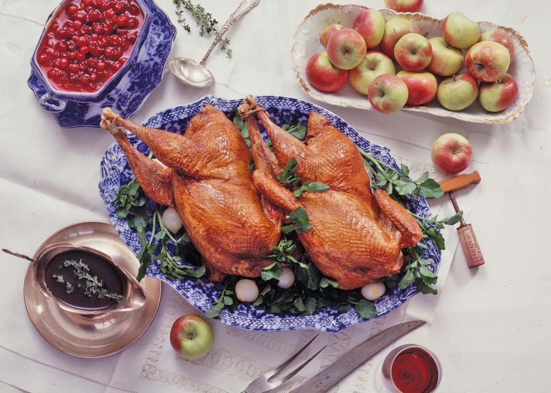 some plated cooked pheasant next to dishes with apples and jams