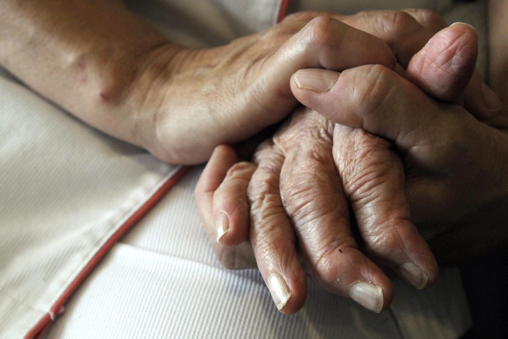 A nurse's hands hold those of an older person with Alzheimer's
