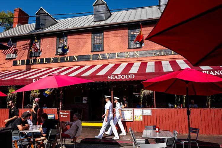 Two U.S. Navy officers stroll past the sunlit Georgian splendor of Middleton Tavern in Annapolis, Maryland. Horatio Middleton established the tavern here in 1750. Today, visitors can order classic Chesapeake seafood, including oysters and rockfish.