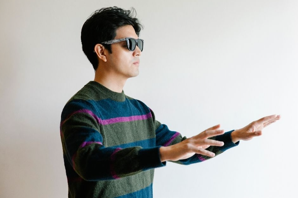 A man wearing sunglasses holds his arms up and in front of him 