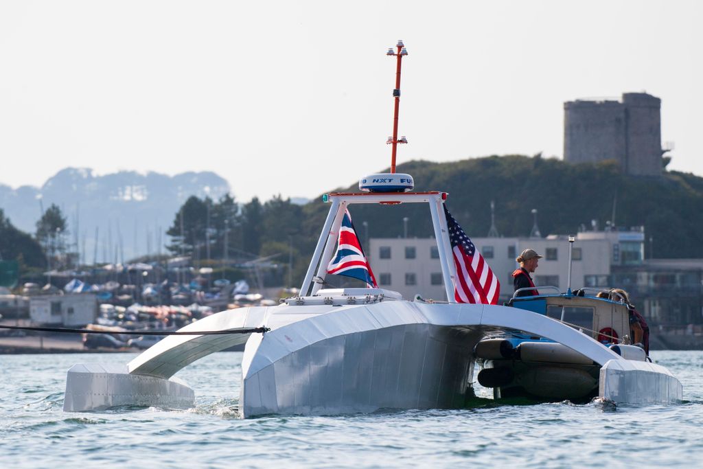 An oddly shaped metal ship with no windows, that floats on top of the water, with an American and British flag, is docked in a harbor