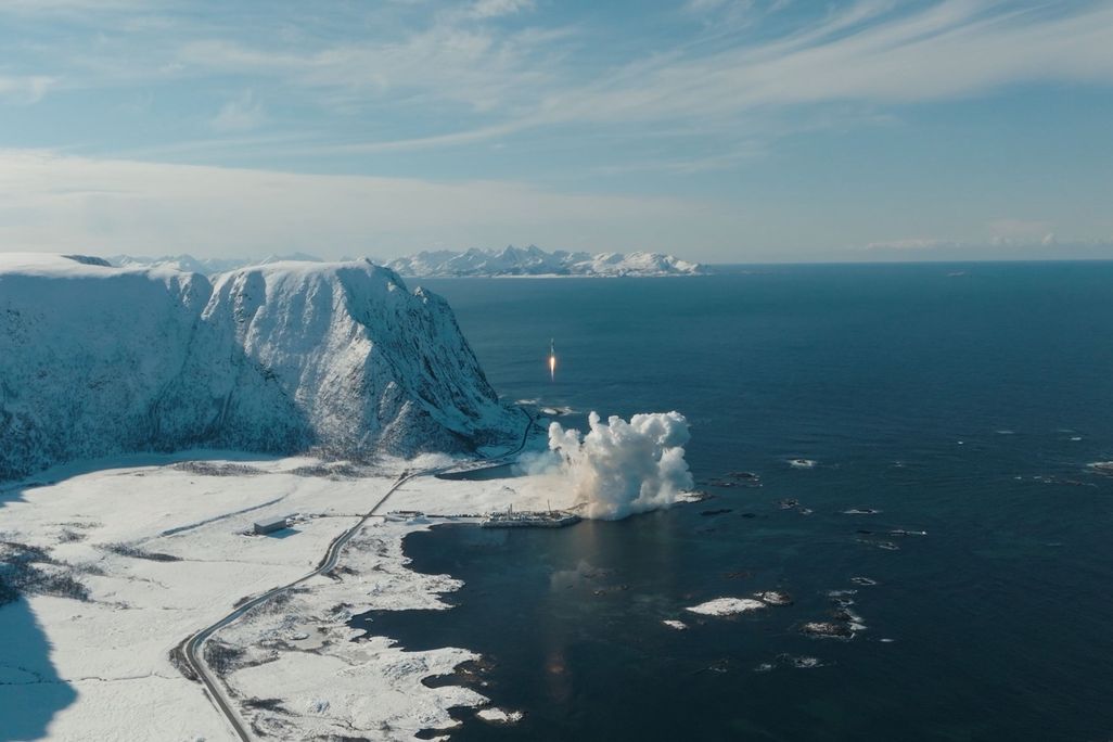 a bird's eye view of a rocket launching near a body of water