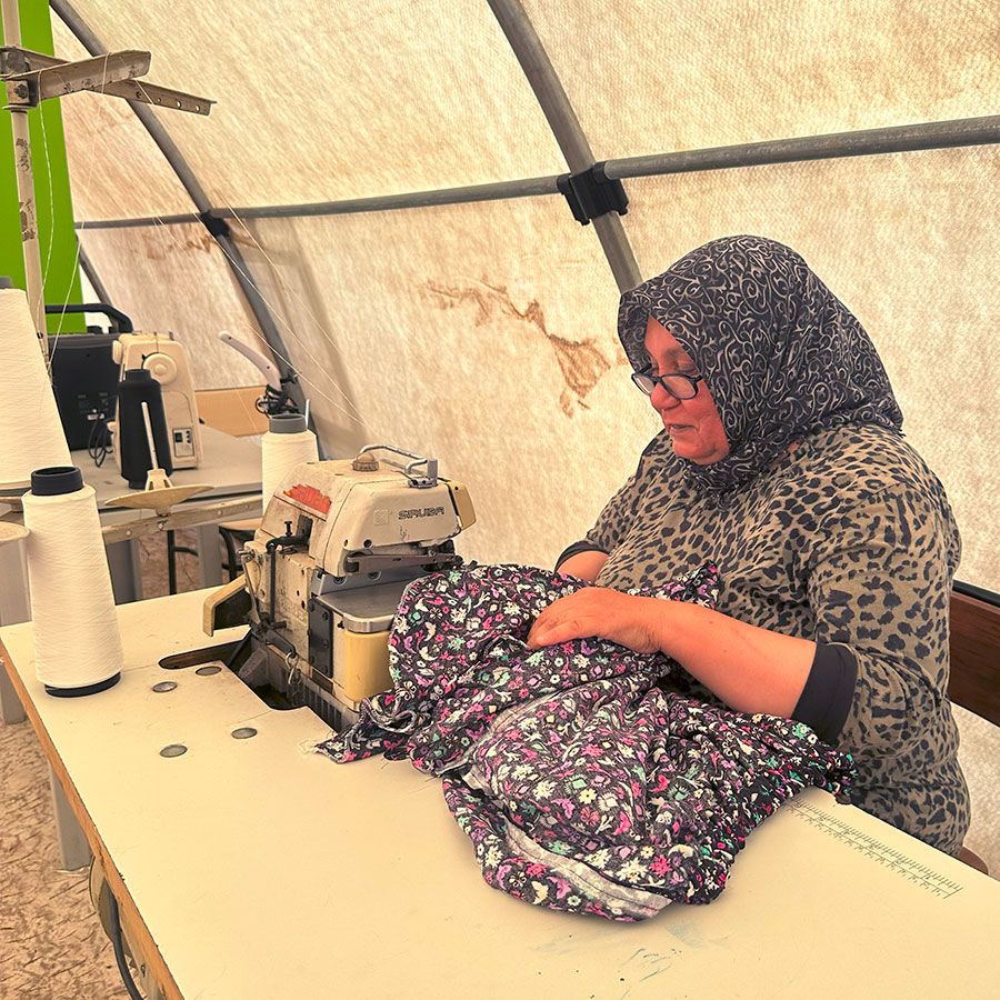 A woman in a headscarf works on a garment on a sewing machine.