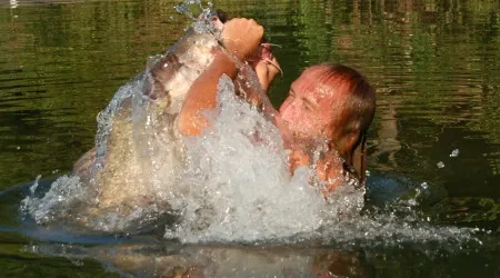David Baggett, famed among noodlers, explodes from the water with a giant catfish in his hands.