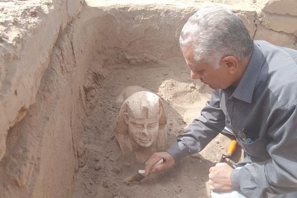 Researcher using a brush to dust off a statue of a sphinx