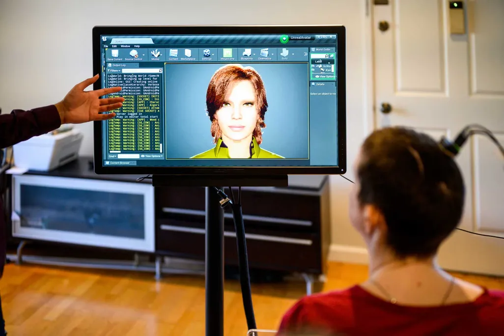 A woman sits facing a computer screen with a digital avatar on it