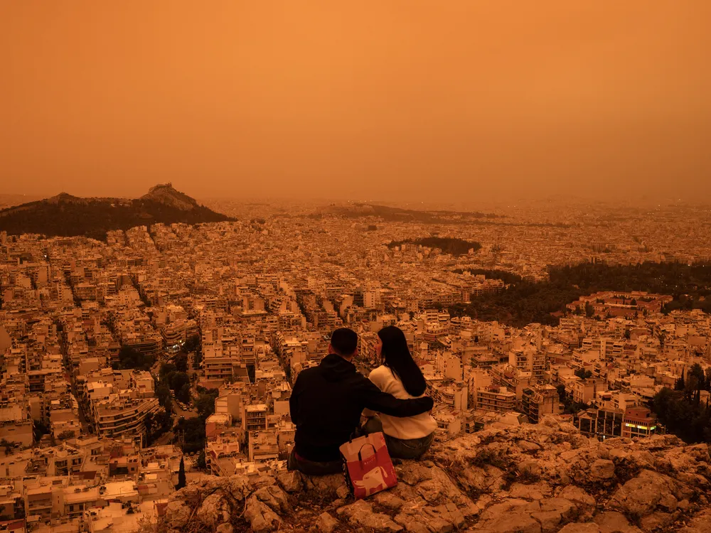 A couple sits atop Tourkovounia hill in Athens, as clouds of Saharan dust cover the capital.