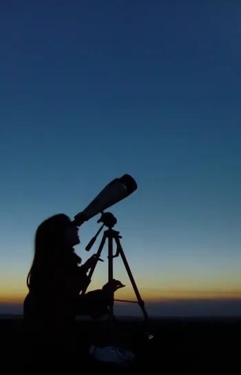 Special Interest Journeys - A silhouette of a woman gazing through a telescope up at the sky during a solar eclipse.
