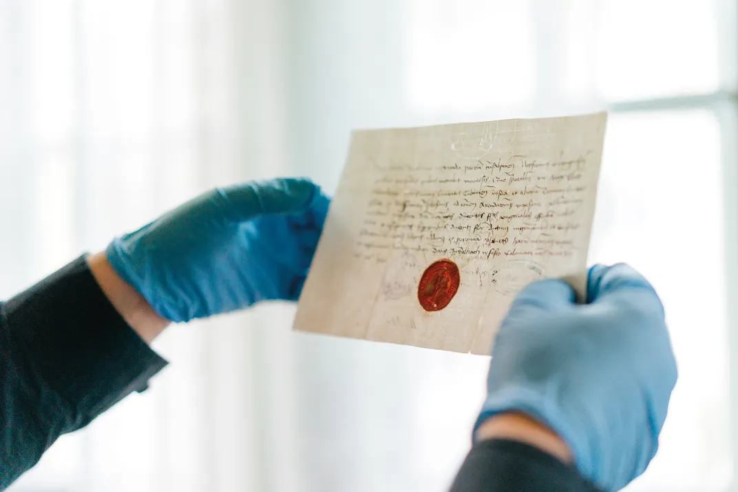 two hands in blue plastic gloves hold up a letter