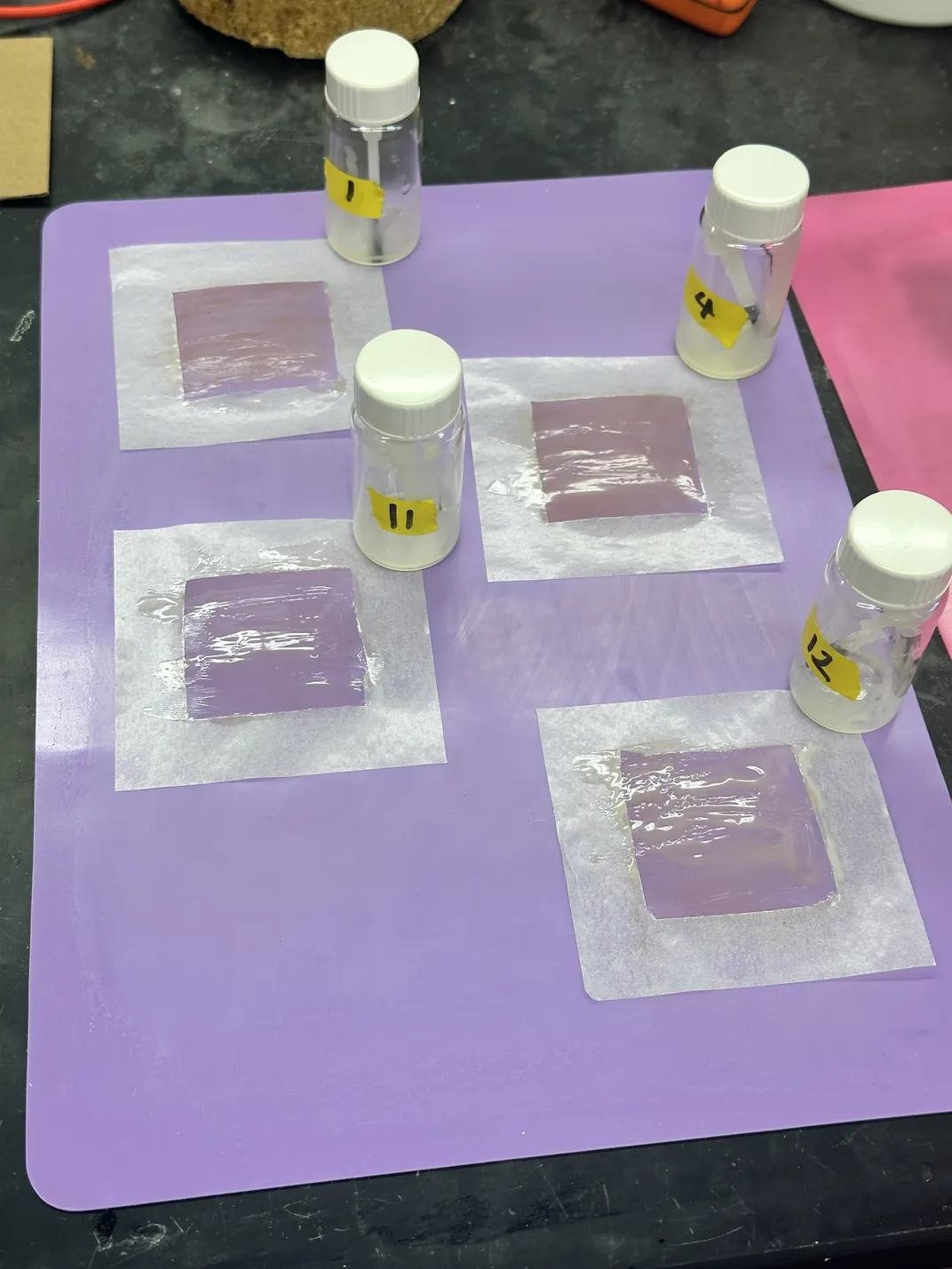 Four bottles on a purple piece of paper with white square on it