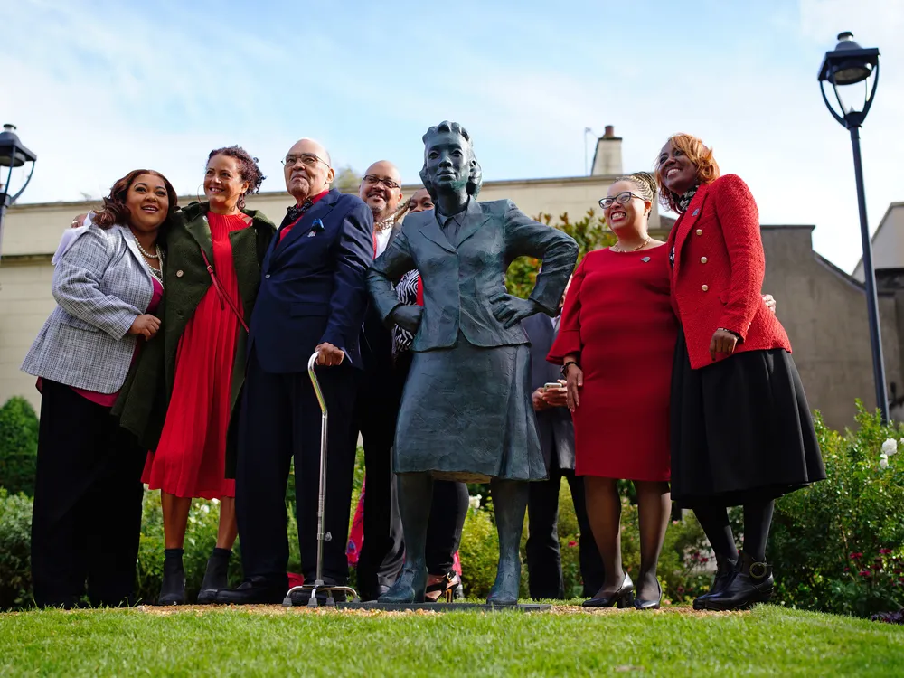 Henrietta Lacks' family stands an grass on either side of a life-sized statue of her