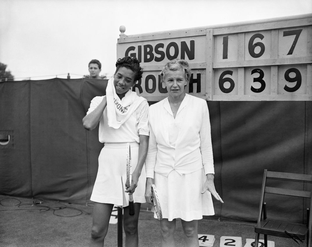 Tennis players Althea Gibson and Louise Brough stand in front of a scoreboard
