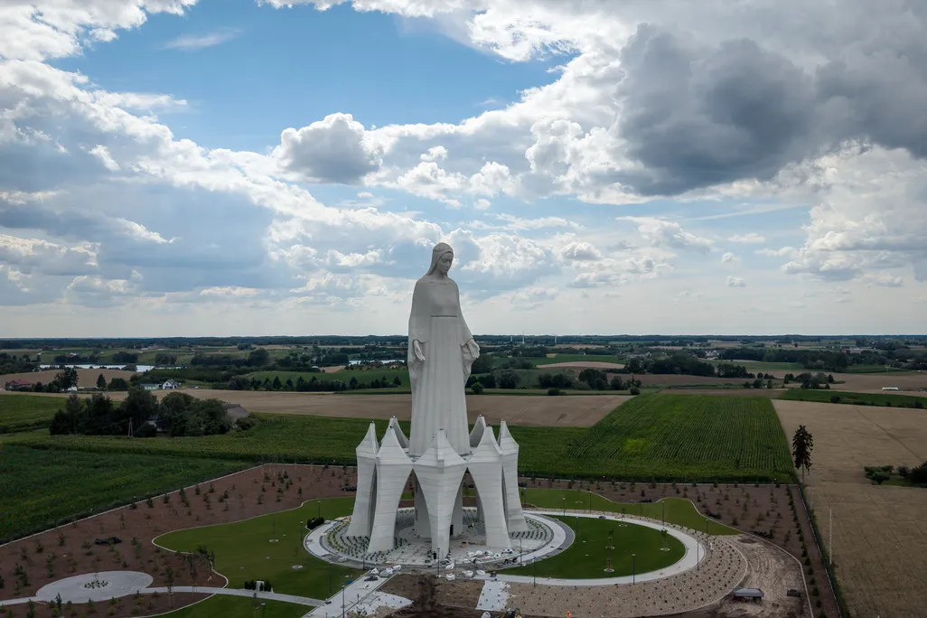 A large statue of the Virgin Mary towering over a field with a sky backdrop