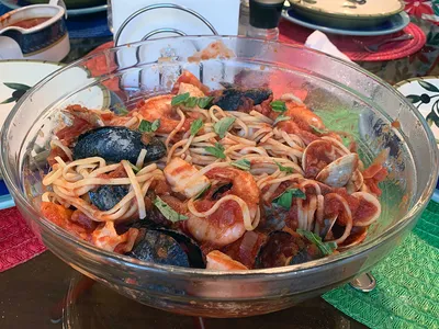 A clear bowl filled with Italian seafood pasta sits on a table with red and green placemats.