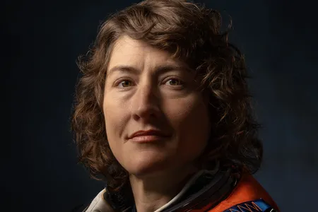 Dramatically-shot portrait of a white female astronaut in an orange spacesuit.