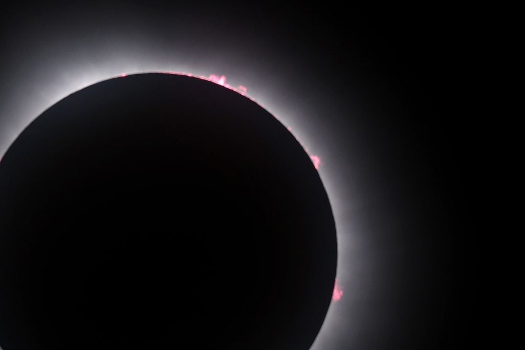 the eclipsed sun in the lower left of the frame shows the corona and some red bits of plasma