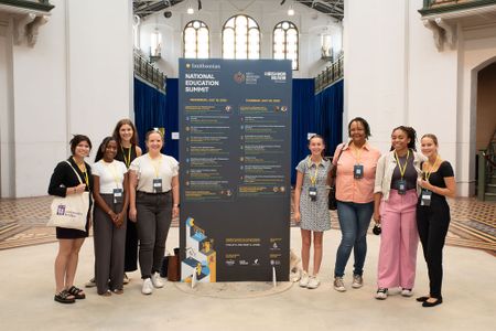 A group of teachers gather around a large blue billboard of the Summit schedule