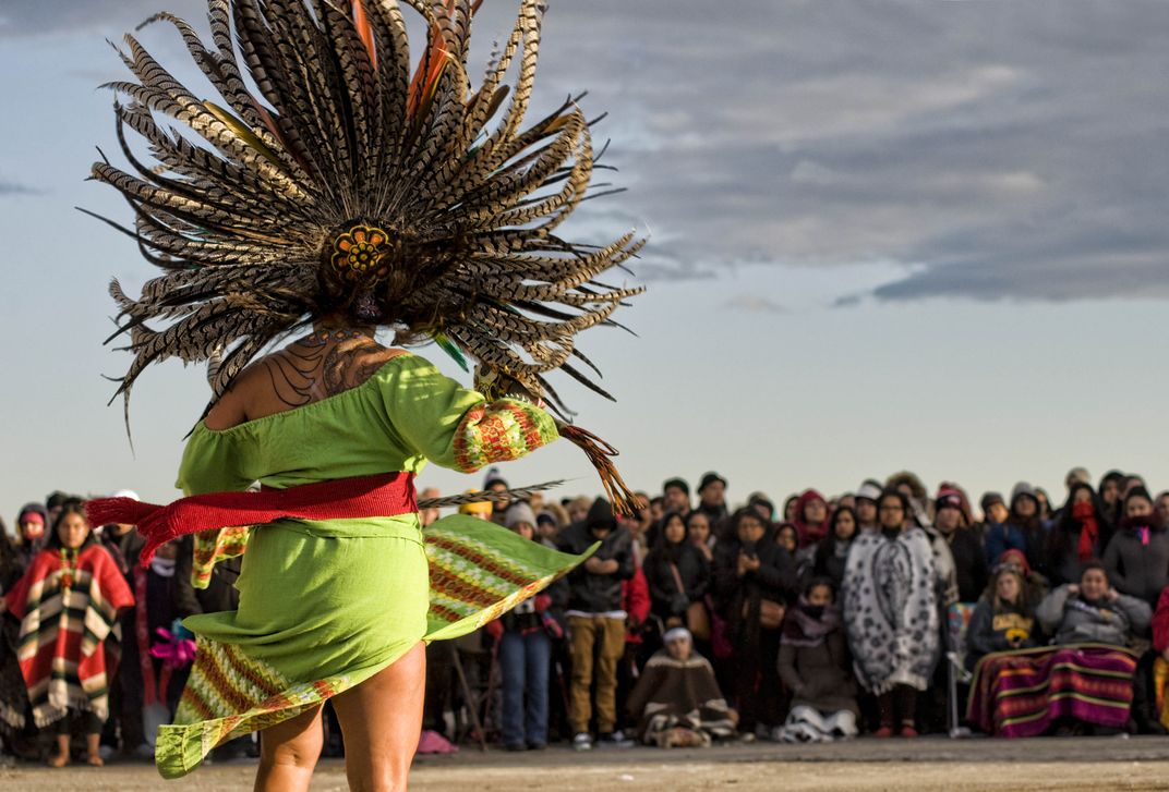 a person in colorful native outfit performs in front of a large crowd
