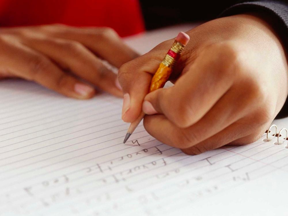 A child writes in a notebook using a pencil in their left hand