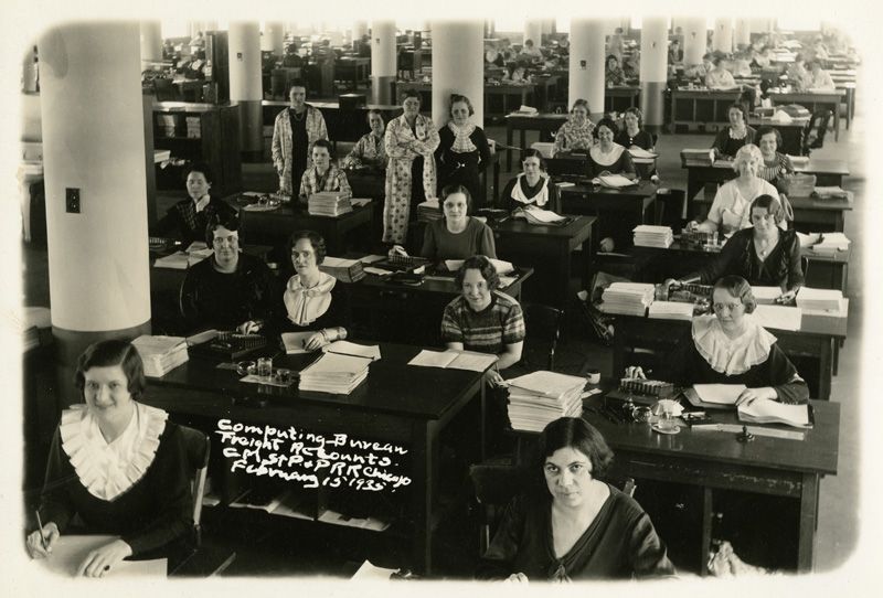 Dozens of women seated behind rows of desks in a large office space
