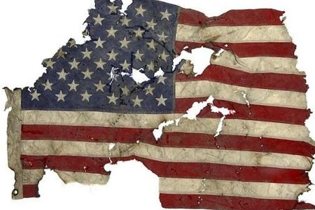 A tattered, torn, and singed American flag displayed against a white background.