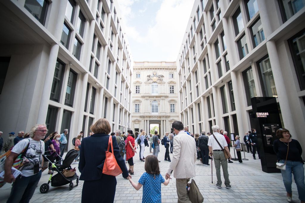A view of the modern entrance to the new museum, with crowds of people walking through a large courtyard surrounded by tall white pillars and windows