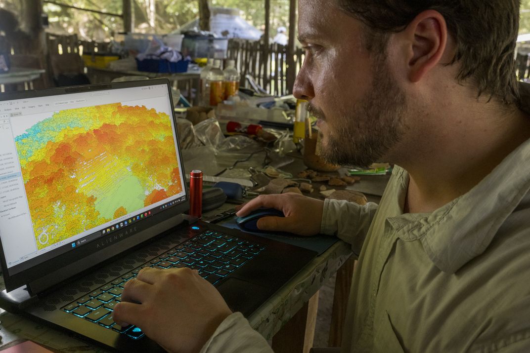 Adrian reviews a lidar image of Caracol. The tree canopy is shown in bright orange, while the lime-colored patch at bottom is Caana, the former home of the royal family. Next year, the team will begin a new round of excavation and stabilizing there.