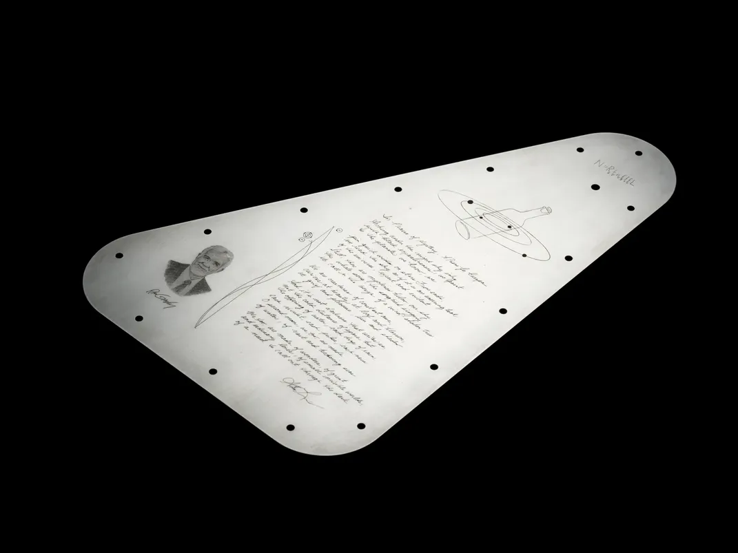 a triangular metal plate with curved edges and holes for screws, demonstrating the engraving of a poem, a portrait, orbiting moons and a mathematical equation