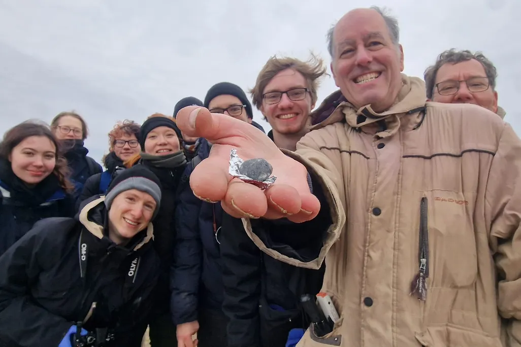 about ten people smiling with one holding a very small rock