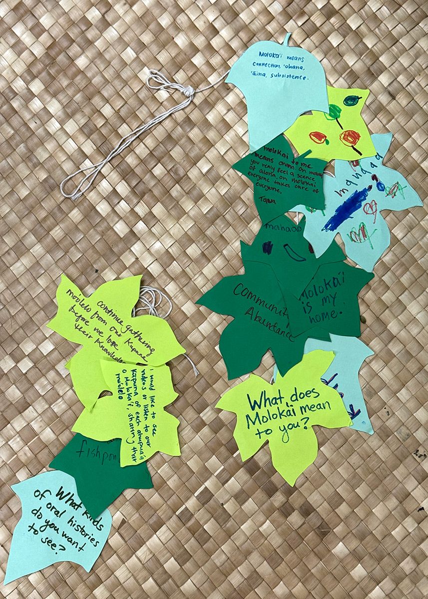 Several green pieces of paper cut into leaf shapes, with words handwritten on them. One reads: What does Molokai mean to you? Another: What kinds of oral histories do you want to see?