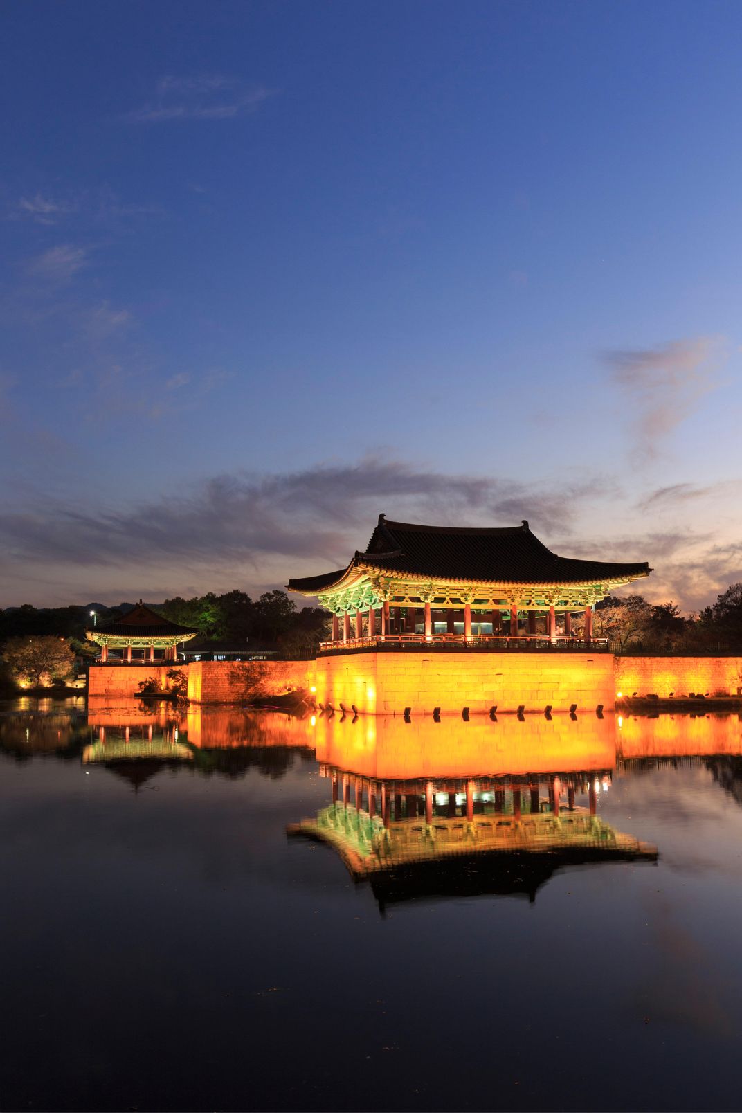 A Korean palace illuminated at night above a pond