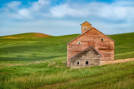 The asymmetrical angles of the roof of this old, abandoned barn complement the scenic rolling hills surrounding it.