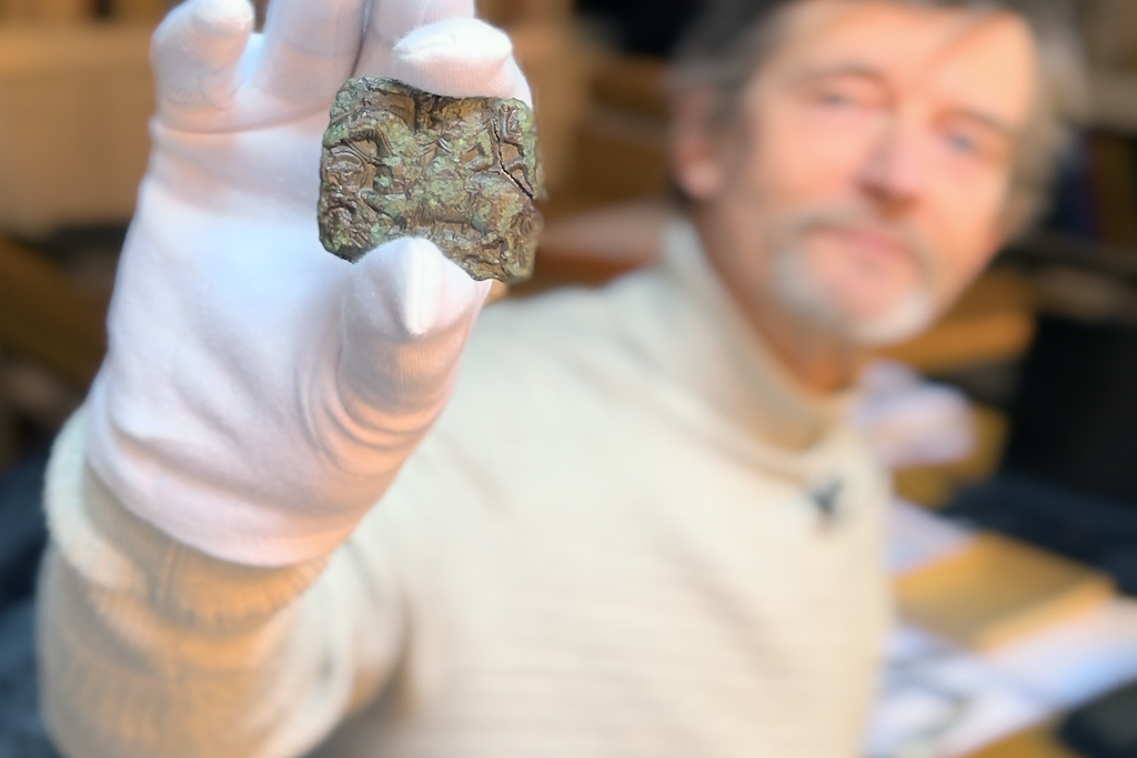 Man in white turtleneck holding up small piece of metal